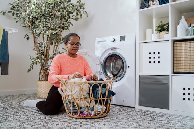 Woman in glasses performs household chores in bathroom laundry room kneels with wicker basket