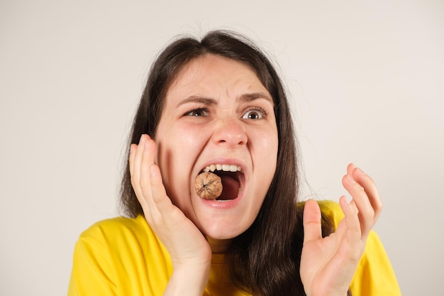 A woman gnaws on a walnut opening her mouth wide