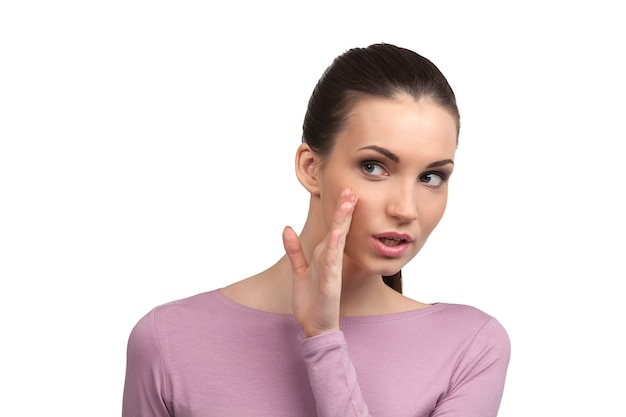 Woman gossiping. Beautiful young woman saying something and holding hand near mouth while standing isolated on white