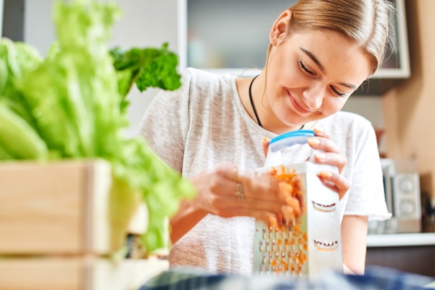 Woman grates the carrots in the kitchen