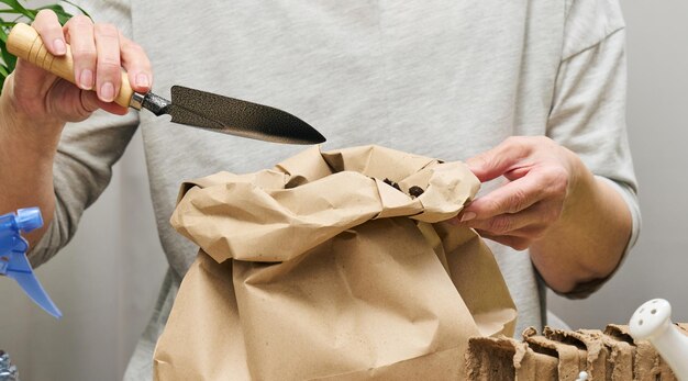 A woman in gray clothes holds a bag of soil for planting seeds in paper cups Hobby and leisure