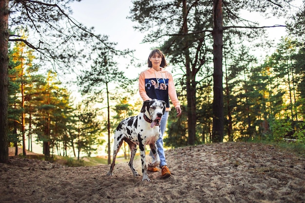 Woman and great Dane dog walking and looking away in forest