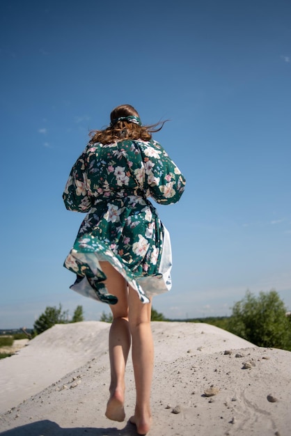 A woman in a green floral dress runs across a sand dune.