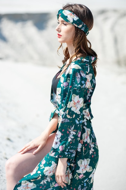 A woman in a green floral dress sits on a rocky beach.