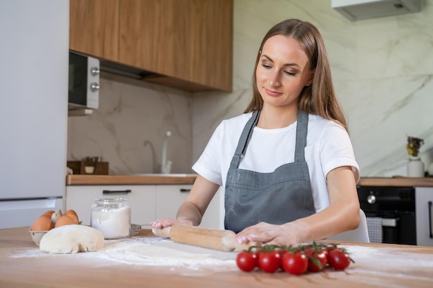 Woman in a grey chef39s apron roll out the dough for preparing pancake Woman rolls out dough