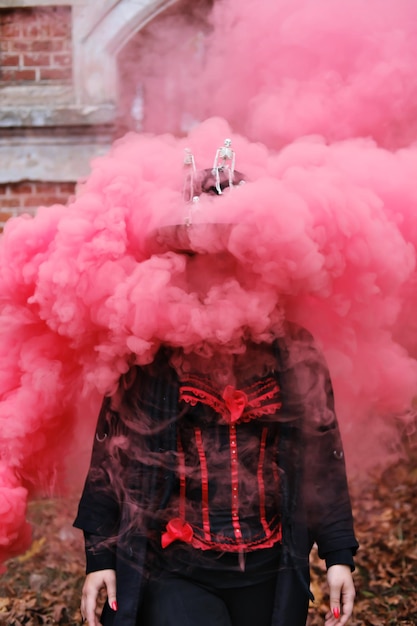 A woman in the guise of Baron Sabbath poses in red smoke Smoke covers the model tightly