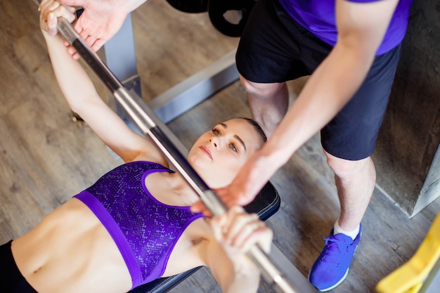 Woman in gym with personal fitness trainer exercising power gymnastics with a barbell.