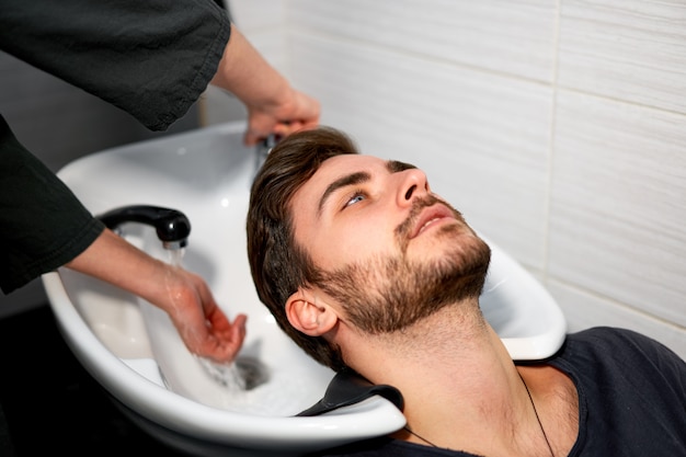 Woman hairdresser wash hair handsome caucasian man in modern barbershop