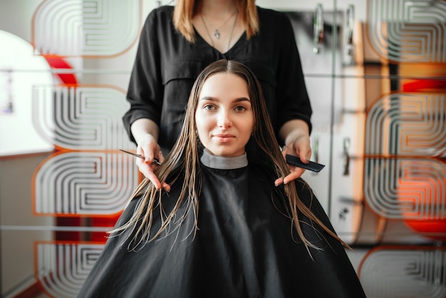 Woman in hairdressing salon, female stylist with scissors and comb in hands