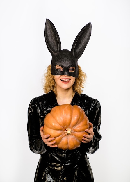 Woman in halloween bunny costume holds pumpkin. Sexy blonde girl in rabbit black mask with pumpkin. Sexy female model in Easter bunny black rabbit mask with jack-o-lantern. Happy Halloween.