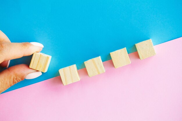 Woman hand arranging empty wood block and copy space on blue and pink background