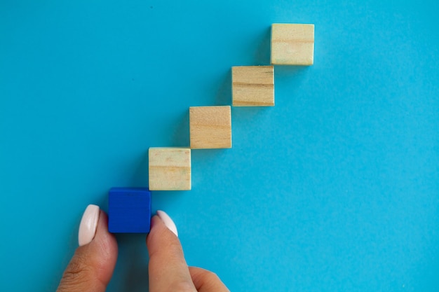 Woman hand arranging empty wood block and copy space on blue and pink background