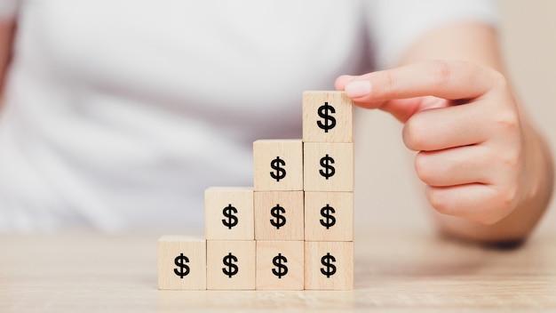 Woman hand arranging wood block with icon money dollar,growth,finance and investment concept.