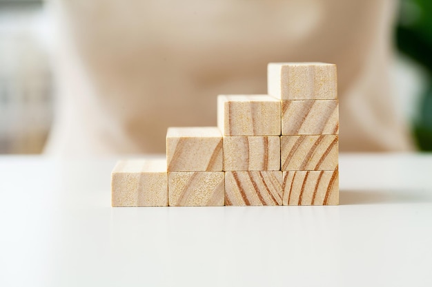 Woman hand arranging wood cube stacking as stair step shape