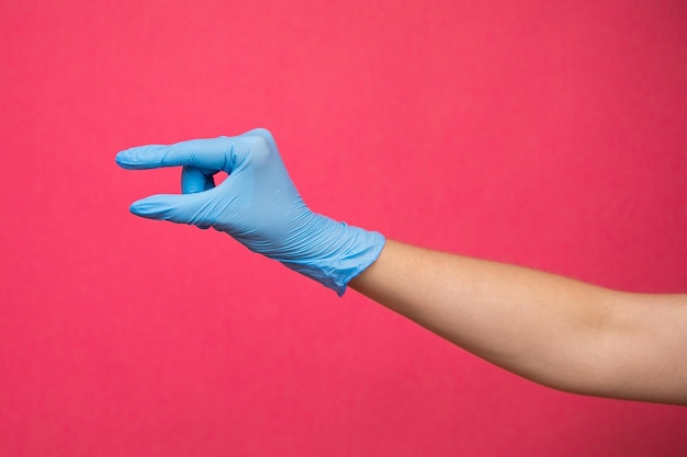 Woman hand in blue medical glove pretending to hold medicine on pink background