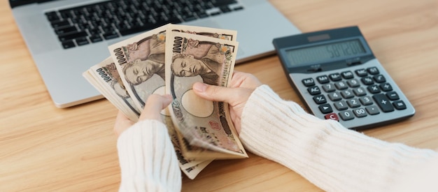 Woman hand counting Japanese Yen banknote with calculator Thousand Yen money Japan cash Tax Recession Economy Inflation Investment finance salary and payment concepts