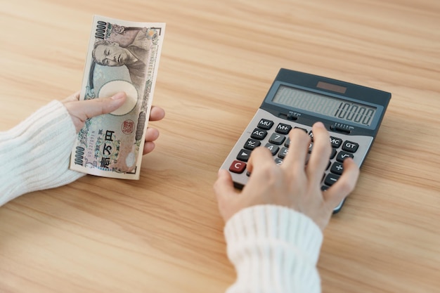 Woman hand counting Japanese Yen banknote with calculator Thousand Yen money Japan cash Tax Recession Economy Inflation Investment finance savings salary and payment concepts