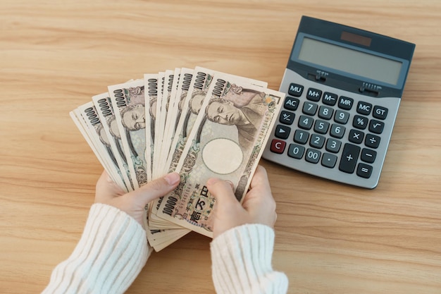 Woman hand counting Japanese Yen banknote with calculator Thousand Yen money Japan cash Tax Recession Economy Inflation Investment finance savings salary and payment concepts