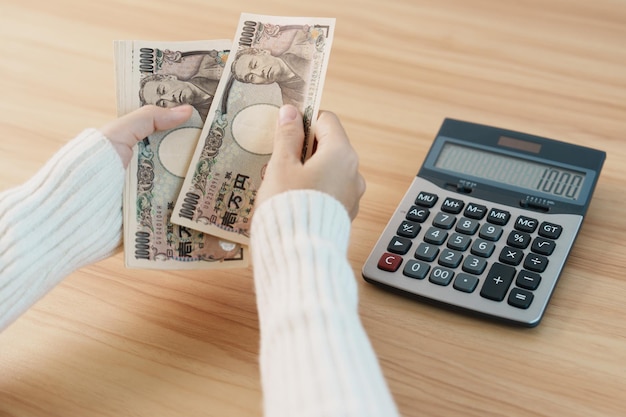 Woman hand counting Japanese Yen banknote with calculator Thousand Yen money Japan cash Tax Recession Economy Inflation Investment finance savings salary and payment concepts