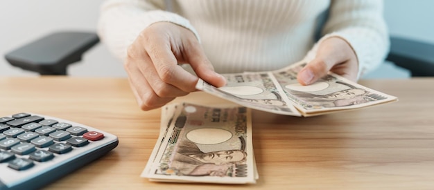 Woman hand counting Japanese Yen banknote with calculator Thousand Yen money Japan cash Tax Recession Economy Inflation Investment finance savings salary and payment concepts