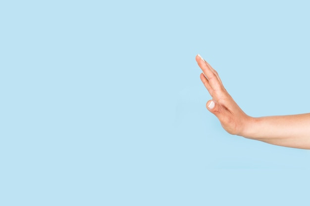 Woman hand doing stop sign on a light blue background with copy space