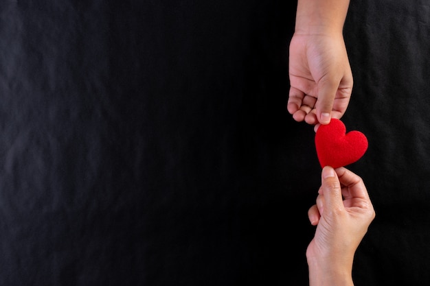 Woman hand giving red heart to child. International day of charity concept. Copy space.