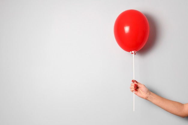 woman hand hold one red  ir balloon in hand on gray background close up