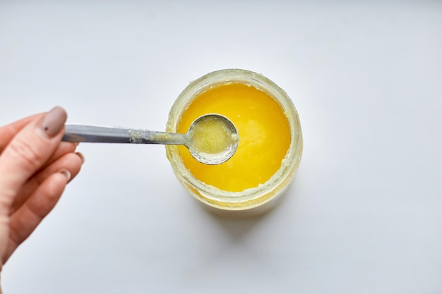 Woman hand hold spoon with ghee oil or clarified butter in jar clarified liquid butter