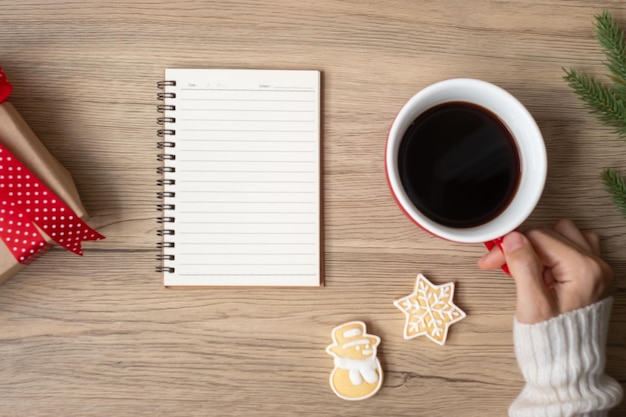 Woman hand holding black coffee cup with blank notebook and Christmas cookies on table Xmas Happy New Year Goals Resolution To do list Strategy and Plan concept