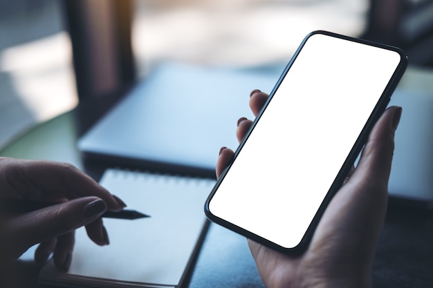 a woman hand holding black mobile phone with blank white desktop screen