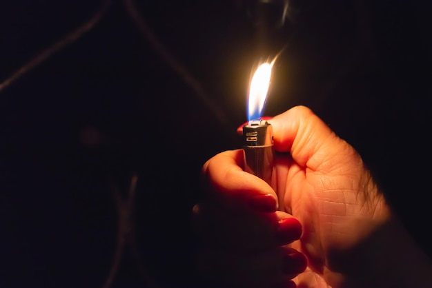 Woman hand holding a burning lighter in the dark black backgroundCloseupselective focusCopy space