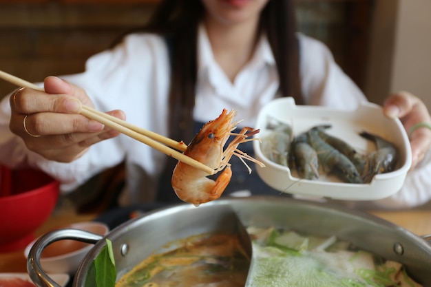 Woman hand holding chopsticks of fresh shrimp with vegetables for cooking or shabu shabu