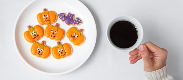 Woman hand holding coffee cup during eating funny Halloween Cookies. Happy Halloween day, Trick or Threat, Hello October, fall autumn, Traditional, party and holiday concept