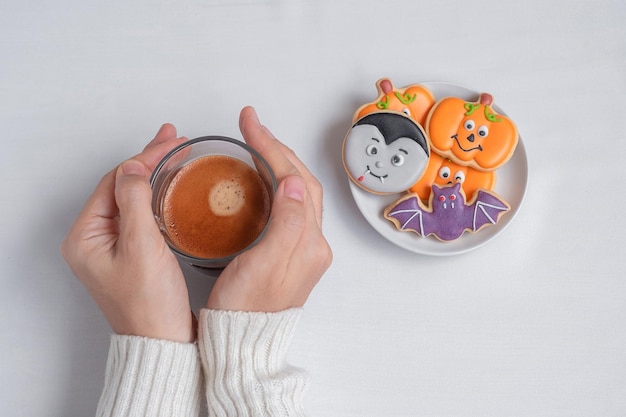 Woman hand holding coffee cup during eating funny Halloween Cookies Happy Halloween day Trick or Threat Hello October fall autumn Traditional party and holiday concept