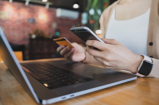 Woman hand holding credit card and using laptop smartphone at cafe for paying online using internet banking service Online shopping concept