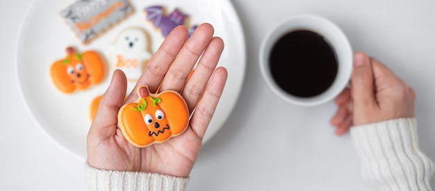 Woman hand holding funny Halloween Cookie during drinking coffee Happy Halloween day Trick or Threat Hello October fall autumn Traditional party and holiday concept