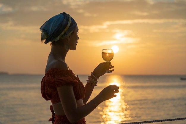 Woman hand holding glass of wine against a beautiful sunset near sea on the tropical beach, close up