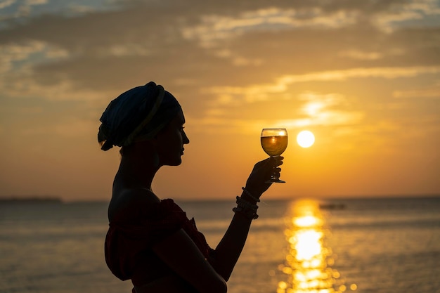 Woman hand holding glass of wine against a beautiful sunset near sea on the tropical beach close up