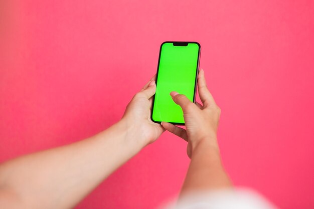 Woman hand Holding a Green Screen Smartphone scroll and touch display on pink background.