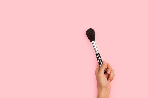 Woman hand holding a make up brush on a pink background with copy space