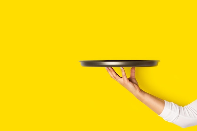 Woman hand holding a metal tray on a yellow background with copy space