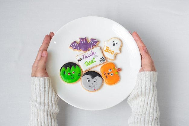 Woman hand holding plate of funny Halloween Cookies Happy Halloween day Trick or Threat Hello October fall autumn Traditional party and holiday concept