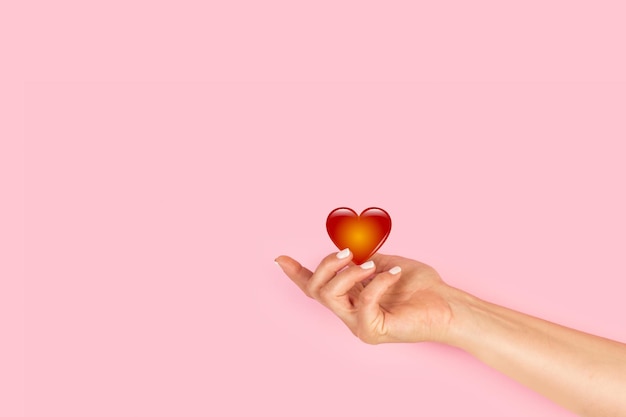 Woman hand holding a red heart on a pink background with copy space