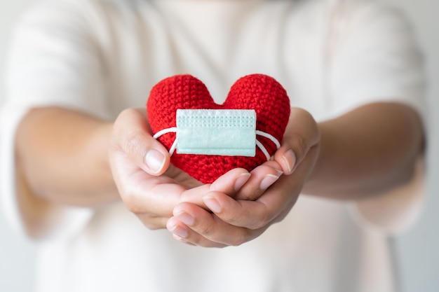 Woman hand holding red heart wearing a protective face mask