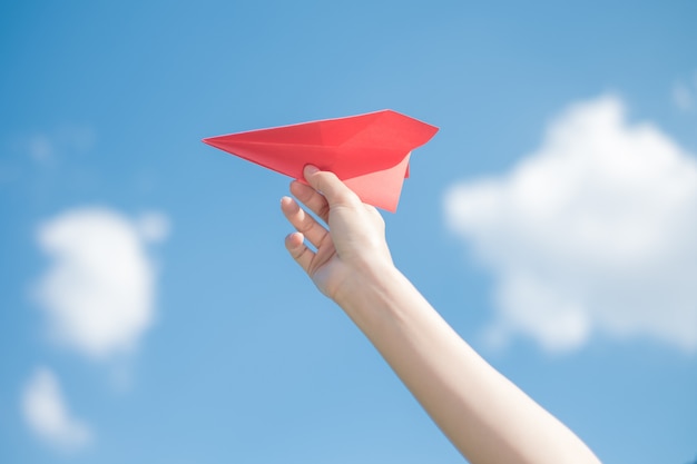 Woman hand holding a red paper rocket with a bright blue background.