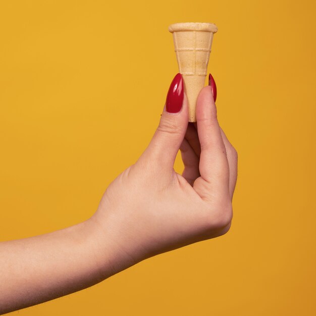 Photo woman hand holding small blank crispy ice cream cone isolated on yellow background