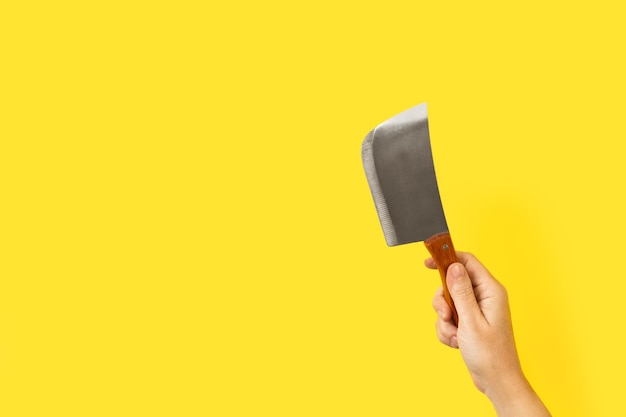 Woman hand holding a small butcher axe on a yellow background