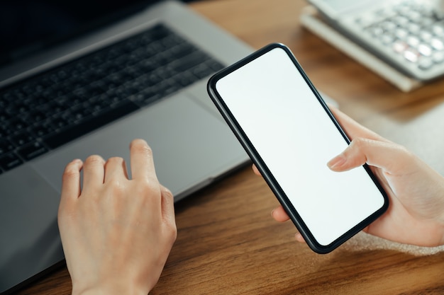 Woman hand holding smartphone with blank copy space screen for your advertisement. laptop on the table.