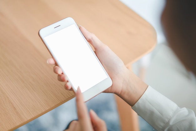 Woman hand holding smartphone with blank screen on table in cafe.