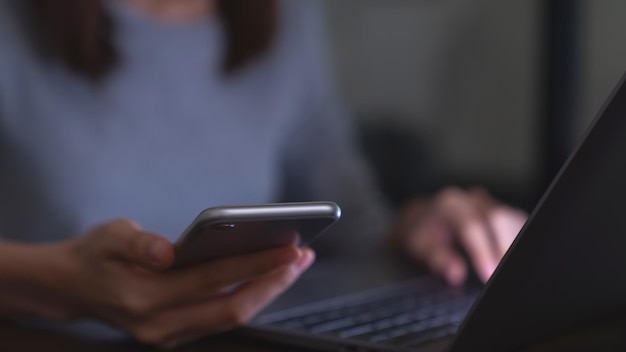 Woman hand holding smartphone with laptop on the table for your advertisement